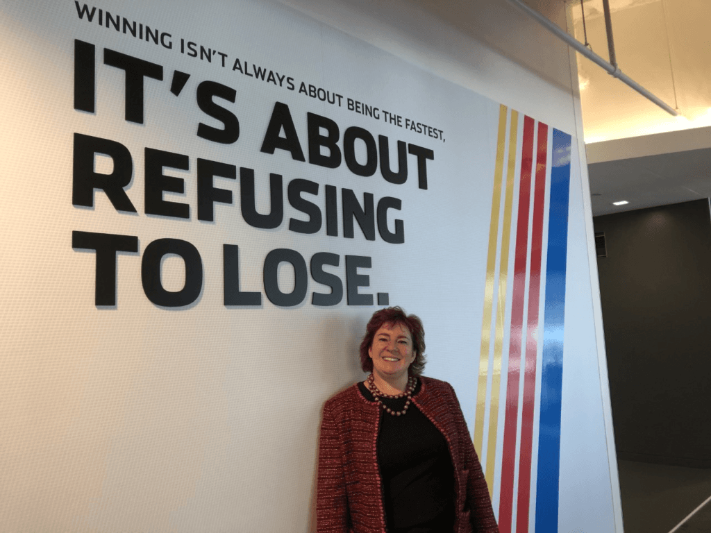 Incendio founder Jenn McMillen in front of mural that states "Winning isn't always about being the fastest, it's about refusing to lose."